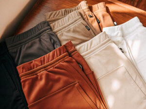 A variety of folded sweatpants in neutral and earthy tones neatly arranged on a wooden surface.