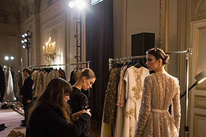Designers and models preparing elegant dresses backstage at a high-end fashion event.