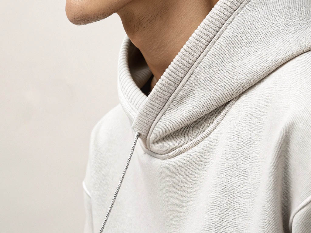 A close-up of a man wearing a beige hoodie, highlighting the ribbed hood, stitching details, and soft fabric texture.