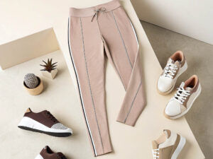 Beige joggers with white side stripes, drawstring waist, and matching sneakers arranged on a neutral-toned background.