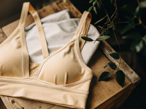 Beige sports bra placed on folded clothes atop a rustic wooden table near green foliage.