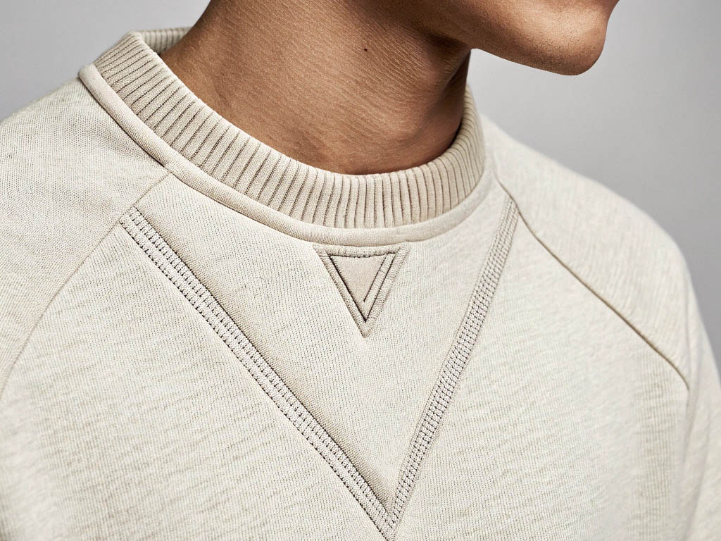 Close-up of a beige sweatshirt with ribbed collar and detailed stitching on the neckline.
