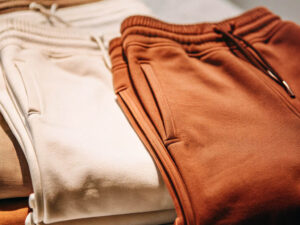 Close-up of neatly folded beige and brown sweatpants with drawstrings, displayed on a clothing store shelf.
