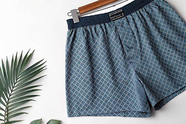 Blue checkered boxer shorts with elastic waistband hanging on a wooden hanger.