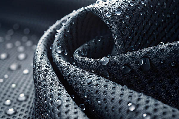 Close-up of dark gray perforated waterproof fabric with water droplets beading on the surface.