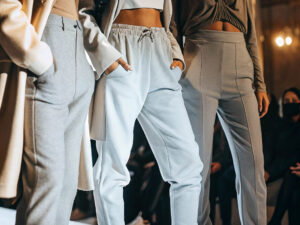 Three models wearing stylish joggers and trousers in neutral tones on a runway.