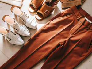Brown tailored pants paired with white lace-up shoes and brown sandals in a stylish flat lay.