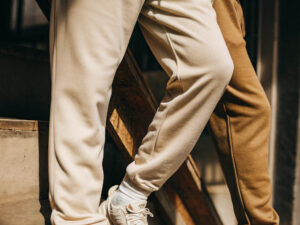 Two people wearing beige and brown sweatpants with sneakers on a wooden staircase.