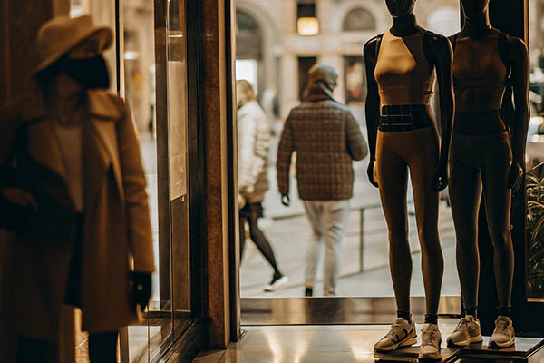 Mannequins in athletic wear displayed near a boutique entrance with shoppers passing by outside.