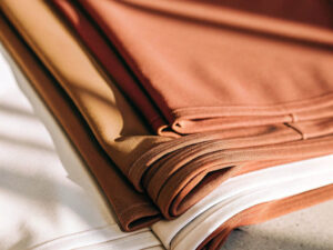Neatly folded casual pants in brown, tan, and cream tones stacked in soft sunlight.