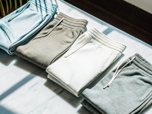 Four neatly folded sweatpants in pastel and neutral tones arranged on a marble surface.