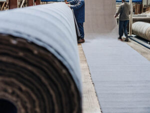 Workers handling a massive roll of fabric in a textile manufacturing facility.