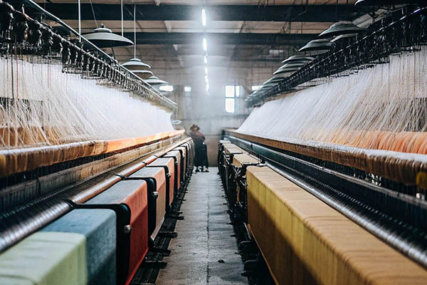 Industrial textile factory with rows of weaving machines producing colorful fabric under overhead lighting.