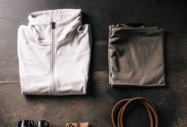 Folded white zip-up hoodie and gray pants with workout accessories on a dark surface.