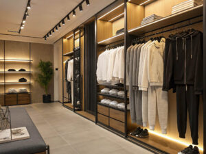 Stylish clothing store with neatly arranged neutral-toned hoodies, sweatpants, and shirts on racks and shelves.