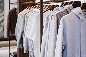 A collection of white and gray hoodies neatly arranged on wooden hangers in a modern retail store.