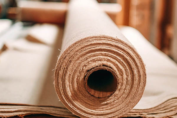 Close-up of a tightly rolled burlap fabric with a rough texture, placed in a workshop setting.