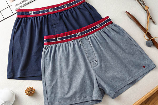 Two pairs of cotton boxer shorts in navy blue and gray with red waistbands.