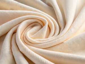 Light cream-colored knit fabric draped in a spiral pattern with a smooth texture.