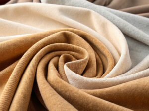 Draped knit fabrics in beige, brown, and gray tones arranged in a swirling pattern.