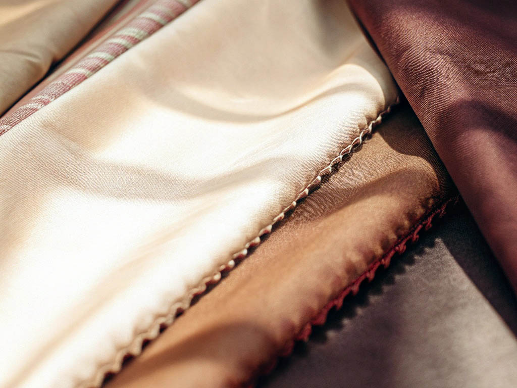 Close-up of layered satin and cotton fabrics in beige, brown, and earthy tones with stitched edges.