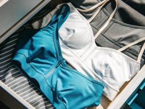 Teal, white, and gray sports bras neatly folded in an open drawer.
