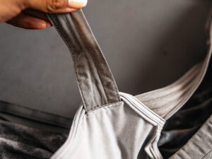 Close-up of a hand holding a gray sports bra strap showing stitching detail.