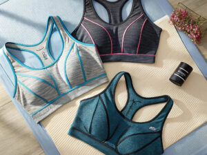 Three colorful sports bras in gray, black, and teal with contrast piping laid on yoga mats.