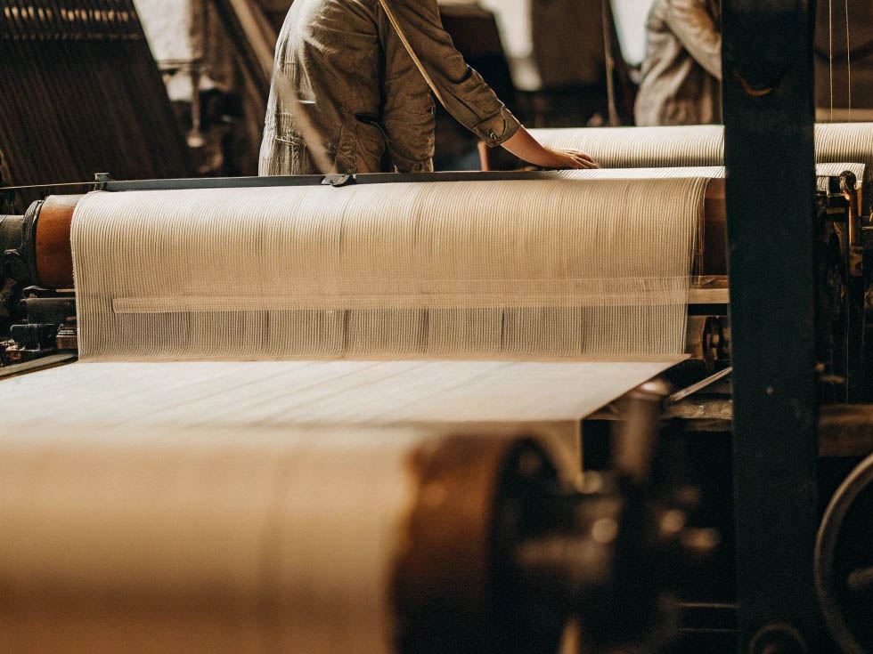 Worker monitoring fabric production on an industrial weaving machine.