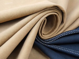 Beige and navy twill fabric neatly rolled and draped, featuring fine stitching details.