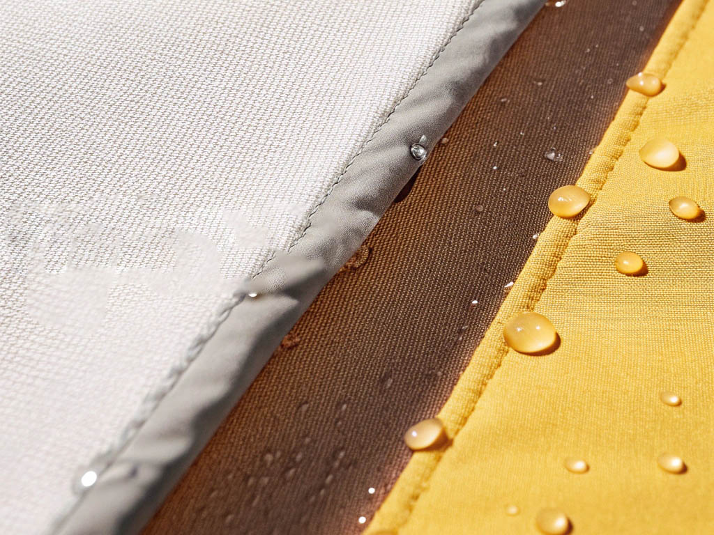 Close-up of waterproof fabric in white, brown, and yellow with water droplets beading on the surface.