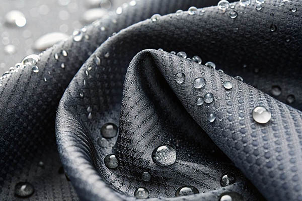 Close-up of dark gray waterproof fabric with water droplets beading on the surface.
