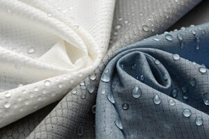 Close-up of white, gray, and blue water-resistant fabric with water droplets beading on the surface.
