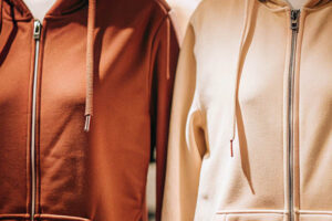 Two zip-up hoodies in warm brown and beige tones, displayed under soft lighting.