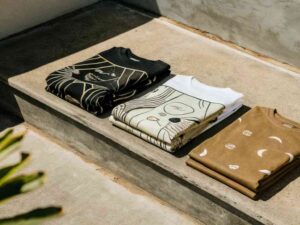 Folded graphic t-shirts with abstract and celestial prints on concrete steps.