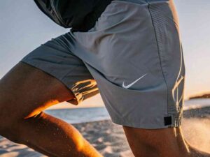 Close-up of a person running on the beach wearing light grey Nike athletic shorts.