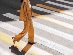 Woman in yellow vest and pants walking on crosswalk