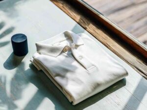 Folded white polo shirt on sunlit table near window