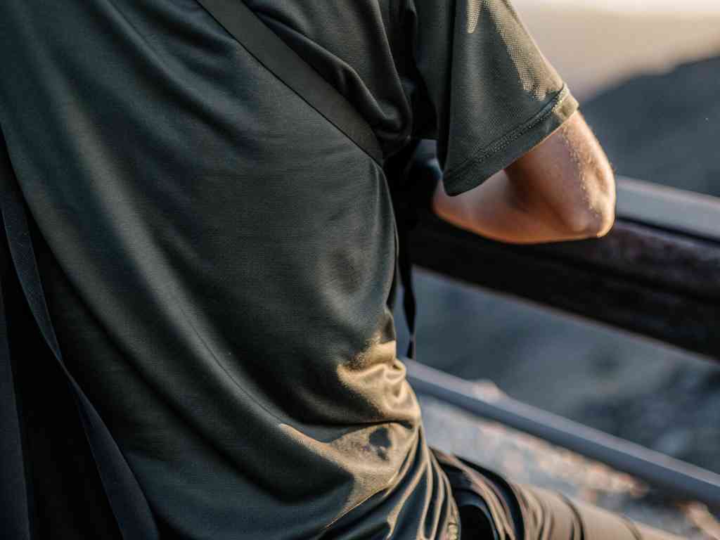 Man in dark green t-shirt leaning on a railing outdoors.