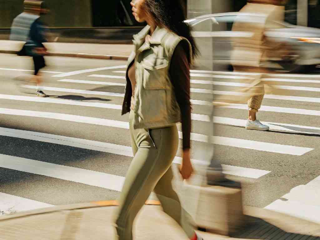 Woman in green vest walking across busy urban crosswalk