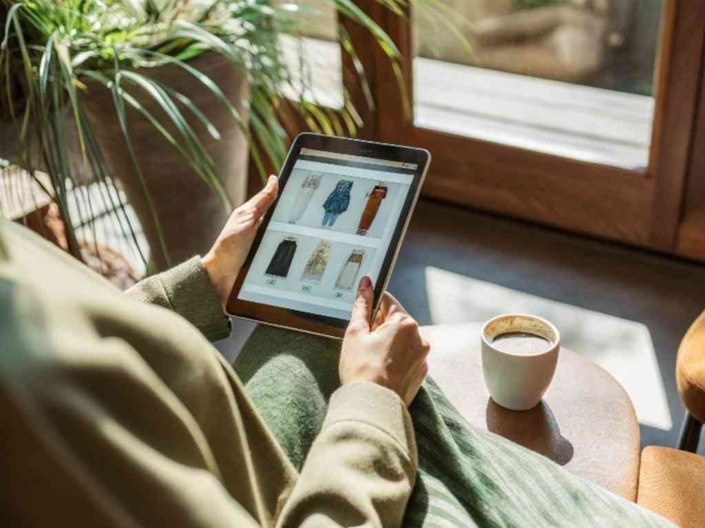 Person browsing online fashion shop on tablet with coffee.