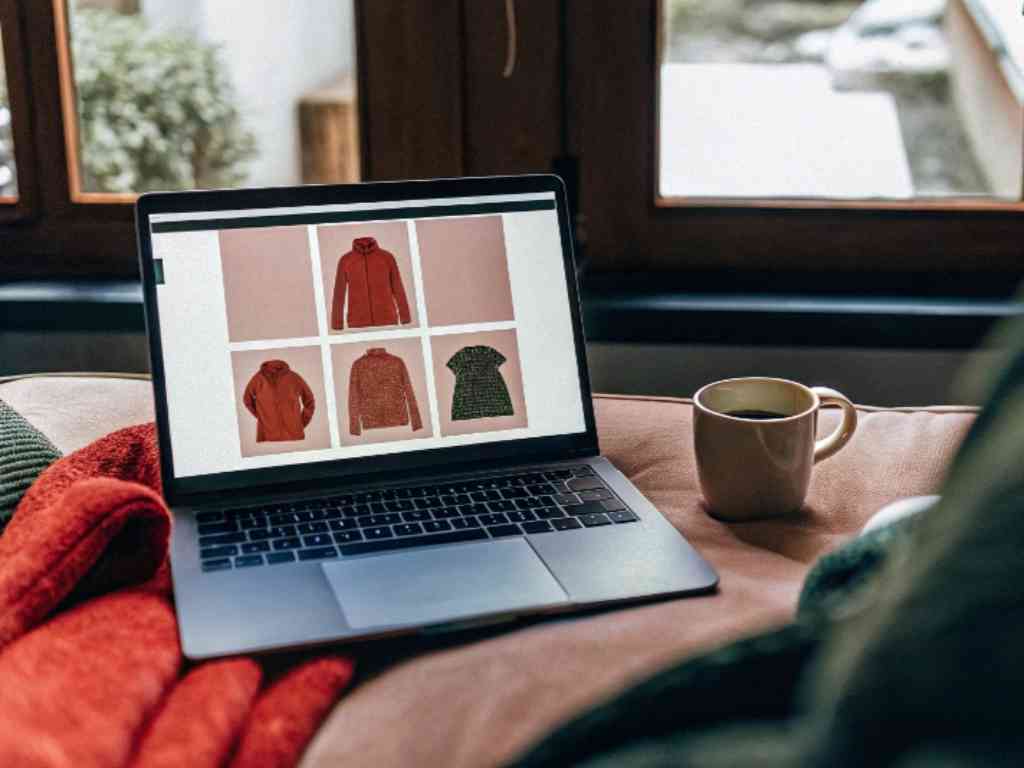 Laptop showing online hoodie and sweater catalog beside coffee cup.