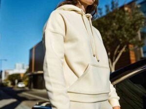 Woman wearing cream-colored hoodie in urban street setting.