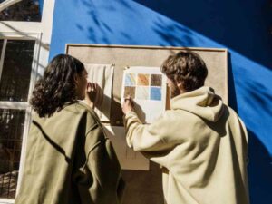 Two creatives discussing fabric swatches on board in sunny studio.