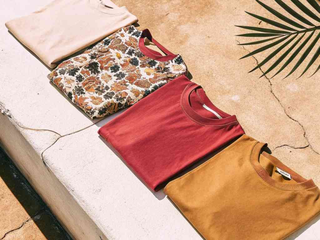 Four folded t-shirts in earthy tones on stone bench