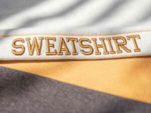 Close-up of soft sweatshirt fabric with gold embroidered "SWEATSHIRT" text.