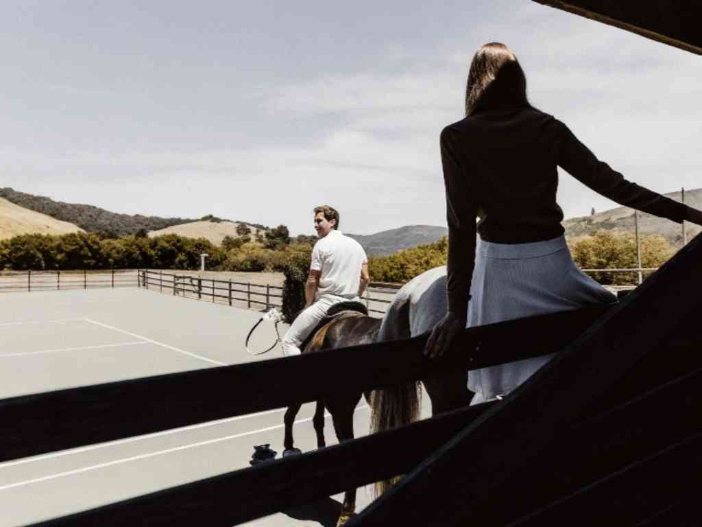Couple on horses overlooking court with scenic mountain backdrop.