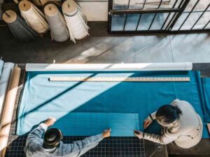 Two designers measuring and marking fabric with ruler and grid.