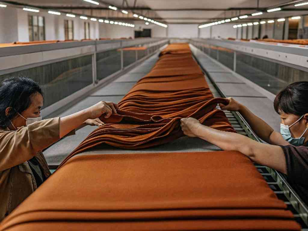 Workers inspecting orange fabric in a textile factory
