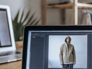 Editing fashion hoodie photos on laptop in cozy studio setup.